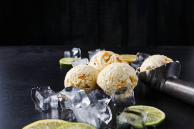 Üç kepçe limonlu ve limonlu dondurma karanlık bir yüzeye konur. Dondurmanın etrafına buz küpleri ve limon dilimleri dizilir. Ortam sıcak bir günde ferahlatıcı bir şeyler öneriyor..