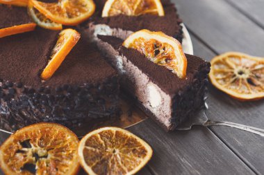 Tahta bir masanın üzerinde duran tatlı parçaları koleksiyonu. Tatlıda çikolata ve krema katmanları var. Kurutulmuş portakal dilimleri üst tarafı süsleyerek tatlı tabağa detay ekler..