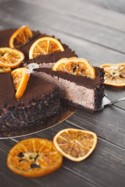 Tatlı koleksiyonunda kuru portakal dilimleriyle dilimlenmiş bir pasta var. Kek koyu ve zengin. Pastayı çevreleyen ekstra kuru portakal dilimleri ahşap bir masanın üzerinde..