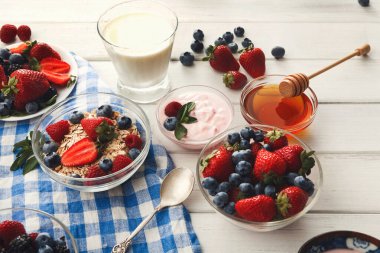 Farklı kaselerde çilek, yabanmersini ve yoğurt var. Yakınlarda bir bardak süt ve bal var. Bu kurgu kahvaltı ya da sıcak bir mutfakta hafif bir yemek için hazır..