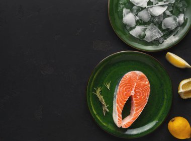 Taze somon bifteği buzla dolu başka bir tabağın yanında yeşil bir tabakta duruyor. Limon ve otlar yakınlarda. Bu ayar yemek hazırlama ya da servis için uygundur.