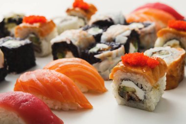 Suşi ruloları ve sashimi beyaz bir tabakta düzenlenir. Kaliforniya dürümleri, somon nigiri ve ton balığı nigiri de dahil olmak üzere farklı suşi türleri mevcuttur. Bu tabak popüler Japon mutfağını ön plana çıkarıyor..