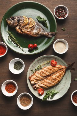 İki balık tabağı yeşil tabağa konur, biri şifalı ve limon dilimli. Tabakları çevreleyen küçük baharat kaseleri ahşap bir masanın üzerinde renkli bir yemek hazırlama sahnesi yaratıyor..