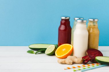 Çeşitli içkilerle dolu cam kavanozlar ahşap bir masanın üzerinde duruyor. Kavanozların yanında portakal, salatalık ve zencefil gibi taze meyve ve sebzeler var..