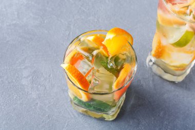 İçi kokteyl dolu iki bardak gri bir yüzeye oturur. İçeceklerde buz var ve portakal ve limon dilimleri ile süslenmiş. Bu sahne genellikle bir barda ya da restoranda bulunur..