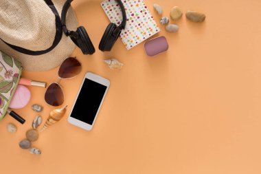 Düz açıda plaj şapkası, kulaklık, güneş gözlüğü, akıllı telefon ve birkaç taş var. Malzemeler turuncu bir yüzeyde güzelce düzenlenir, su kenarında bir gün için hazırdırlar..