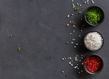 Çeşitli baharatlar karanlık bir yüzeyde küçük kâselerde sıralanır. Yeşil otlar, beyaz tuz ve kırmızı biberler görülebilir. Biraz baharat kâselerin etrafına saçılmış..