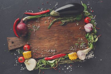 Bir kesme tahtası çeşitli taze sebzeler ve otlarla çevrilidir. Kırmızı biber, domates, mısır ve yapraklı yeşiller renkli bir görüntü oluşturur. Sahne yemek hazırlığı öneriyor..
