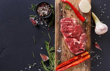 Taze et parçaları ahşap bir tahta üzerinde çeşitli baharatlar, otlar ve sarımsak ile düzenlenir. Kırmızı biber ve tuz da mevcut. Bu sahne bir mutfakta yemek pişirme sürecini yakalar..