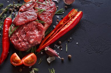 Siyah bir yüzey üzerinde taze et parçaları otlar, kırmızı biber, domates, sarımsak ve baharatlarla gösterilir. Ayarlar yemek hazırlığını gösteriyor. Çeşitli malzemeler düzgünce düzenlenmiş..