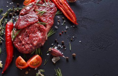 Çiğ et taze baharatlar, otlar ve sebzelerle çevrili karanlık bir yüzeye yerleştirilir. Biber, domates ve sarımsak içeriyor. Bu kurgu yemek hazırlamak için..