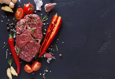 Kırmızı et dilimleri domates, kırmızı biber, sarımsak, zencefil ve otlarla birlikte koyu bir yüzeye yerleştirilir. Bu kurulum yemek veya yemek hazırlığı için gerekli malzemeleri gösterir.