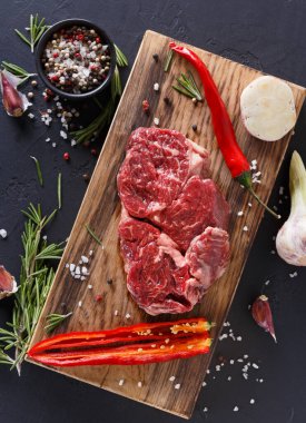 Taze et kesikleri ahşap bir tahtaya yerleştirilir. Etin etrafında sarımsak, otlar ve renkli kırmızı biberler var. Siyah biberler ve kaba tuz bu sahneye tat katar..