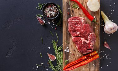 Taze et ve renkli sebzeler ahşap bir kesme tahtasında düzenlenir. Sarımsak, biber ve otlar etin etrafını sarmış, yemek hazırlamak için gerekli malzemeleri gösteriyor..