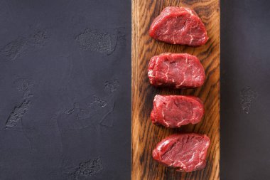 Tahta kesme tahtasına dört parça taze et konur. Arka plan karanlık, ve yemek yapmaya hazır çiğ ete odaklanmış durumda..