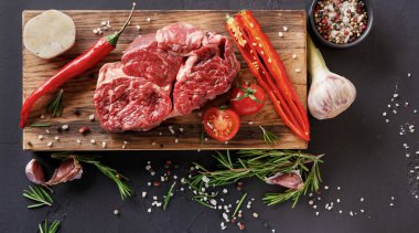 Taze et parçaları kırmızı biber, sarımsak, domates ve bitkilerle çevrili ahşap bir kesme tahtasına konur. Kurulum, etrafa saçılmış baharatlarla yemek pişirmeye hazır bir mutfak gösteriyor..