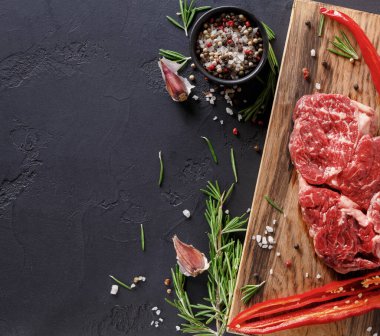 Kesme tahtasında biberiye, sarımsak ve kırmızı biber filizlerinin yanında taze çiğ et sergileniyor. Küçük bir kase renkli biberli mısır karışımı içerir. Sahne karanlık bir yüzeye kurulmuş..