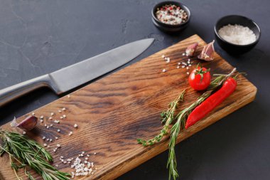 Mutfak tezgahına yanında bıçak olan bir kesme tahtası konur. Taze bitkiler, kırmızı biber, tuz ve sarımsak tahtaya güzelce yerleştirildi..