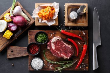 Taze sebzeler, otlar ve et bir mutfaktaki ahşap bir tahtada düzenlenir. Bıçak yakına konur ve baharatlar kâselerin içindedir. Bu sahne yemek hazırlıklarını gösteriyor..