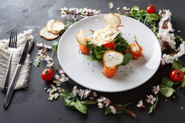 Somon, yeşillik ve otlardan oluşan beyaz bir tabakta bir salata düzenlenir. Tabağın etrafına vişneli domates ve dilimler konur. Dekoratif çiçeklerle kaplanmış karanlık bir yüzeye kurulmuştur..