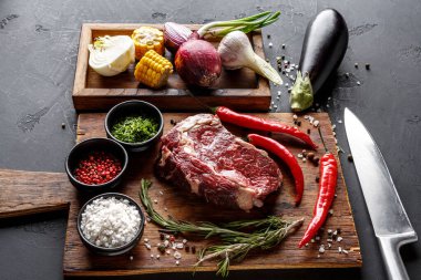 Tahta kesme tahtası, sebze ve baharat seçiminin yanında taze et tutar. Kırmızı biber, soğan, mısır ve otlar yemek hazırlığı için düzenlenir. Yakınlarda bir bıçak var..