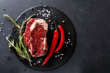 Bir parça çiğ et, kırmızı biber ve taze biberiyeyle siyah taş bir yüzeye yerleştirilir. Beyaz ve siyah biberler etrafa saçılmış. Hazırlıklar yemek hazırlamak için..