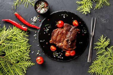 Izgara et siyah bir tabağa konur. Taze vişneli domatesler etin etrafını sarmış. Yeşil otlar ve kırmızı biberler renk katar. Baharat yakınlardaki küçük bir kasede..