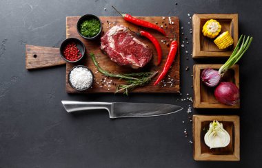 Tahta kesme tahtasında kırmızı biber, şifalı otlar ve çeşitli sebzelerle çevrili bir biftek dilimi bulunur. Baharatlı, yeşillikli ve mısırlı kaseler sahneye detay ekler..