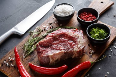 Çiğ sığır eti, otlar, baharatlar ve kırmızı biberlerle çevrili ahşap bir tahtanın üzerinde oturur. Yakınlardaki küçük kaselerde tuz ve biber var. Bıçak tahtanın yanına konur, yemek pişirme sahnesi yaratır..