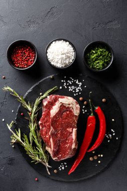 Çiğ bir et parçası yuvarlak siyah bir tabakta oturur. Kırmızı biber, tuz ve baharatlar yakınlardaki küçük kaselerde düzenlenir. Taze bitkiler olay yerine renk katar. Bu da yemek hazırlığını gösterir..