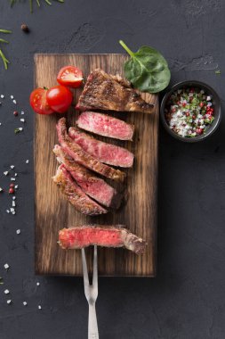 Sulu biftek dilimleri ahşap bir tahtada güzelce düzenlenir. Kiraz domatesleri ve bir kase baharat etin yanında oturur. Dekor koyu yüzeyi olan bir mutfak..