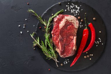 Bir parça çiğ et karanlık bir yüzeye yerleştiriliyor. Yanında bitkiler ve kırmızı biberler var. Ayarlar yemek pişirme hazırlıklarını gösteriyor. Tuz ve biber olay yerine detay ekler..