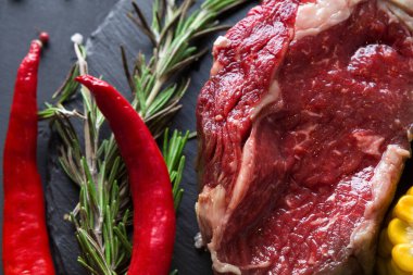 Bir parça çiğ et siyah bir yüzeye yerleştirilir. Yakınlarda kırmızı biber, hardal ve biberiye filizleri var. Bu kurulum mutfakta yemek hazırlığı için hazır..