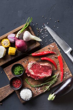Taze et ve sebzeler ahşap tahtalarda düzenlenir. Biftek, baharat ve çeşitli sebzeler var. Yakınlarda bir bıçak var, yemek hazırlığı için hazır..