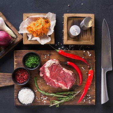 Tahta bir masada, soğan, bitki, biber ve baharatla birlikte çiğ et var. Bazı sebzeler küçük kaselerde hazırlanır. Yakınlarda tuzluk ve biberlikler var. Masanın üzerinde de bir bıçak var..