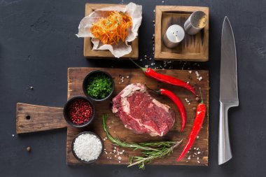 Tahta, taze otlar, baharatlar ve sebzelerle birlikte çiğ et kesimini de sergiler. Tahtada bir bıçak ve baharat kapları da var. Bu sahne yemek hazırlıklarını gösteriyor..