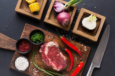 Taze biftek, doğranmış sebze ve otların yanında ahşap bir tahtaya konur. Kırmızı soğan, mısır ve baharatlar küçük kaselerde sıralanır. Yakınlarda bir bıçak duruyor, hazırlanmaya hazır..