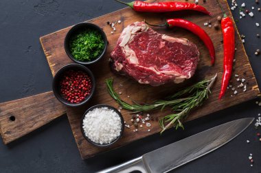 Çiğ bir biftek parçası ahşap bir kesme tahtasına yerleştirilir. Bifteğin etrafında kırmızı biber, bir kase şifalı ot ve tuz var. Yakınlarda bir bıçak var, hazırlanmaya hazır..