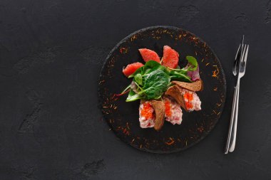 Karides, salata yeşillikleri, ekmek ve greyfurt içeren bir tabak siyah bir tabağa yerleştirilir. Tabağın yanında iki çatal var, yemek deneyimi için hazırlıyorlar..