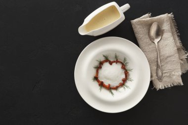 Beyaz bir tabak, sos ve bitkilerden oluşan dairesel bir dizayn ile düzenlenir. Soslu bir sos kabı katlanmış bir bez ve bir kaşığın yanında oturur. Ayarların koyu bir arkaplanı var.