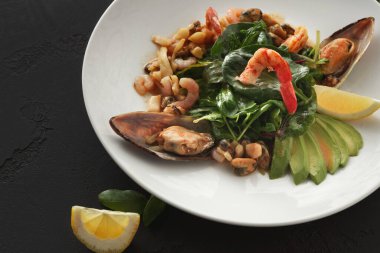 Karides, midye ve çeşitli sebzelerden oluşan bir deniz ürünleri tabağı. Tabak limonla süslenir ve beyaz bir tabakta sunulur, canlı renkler sergilenir..