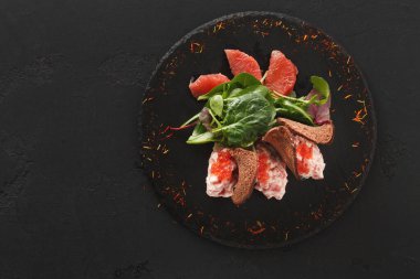 İçinde greyfurt dilimleri, taze yeşiller ve koyu bir tabakta sunulan ekmekle servis edilen kremalı bir karışım olan bir salata. Bu yemek bir yemek masasında düzgün bir şekilde sunuluyor..