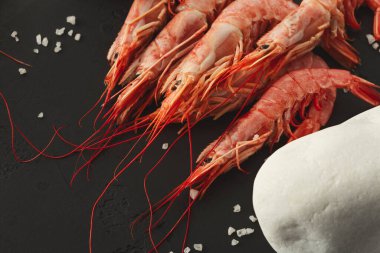 Çiğ karides karanlık bir yüzeye serilir. Etraflarına birkaç tuz tanesi saçıldı. Karidesin yanına bir taş yerleştirilir ve basit ekrana eklenir..