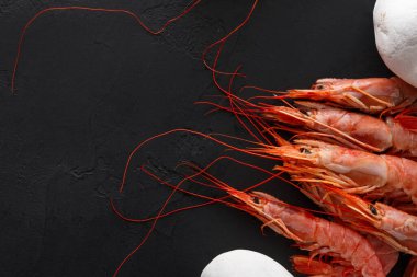 Uzun kuyruklu ve parlak renkli karides koyu bir yüzeye yerleştirilir. Beyaz malzemeler karidese yakın görünüyor. Bu da yemek hazırlığı olduğunu gösteriyor..