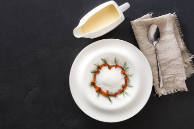 Bir yemek, kremayla ve otlarla süslenmiş dairesel bir desenle düzenlenir. Sosun bir tarafı küçük bir tabakta sunulur. Yakınlarda bir kaşık ve bez peçete var..