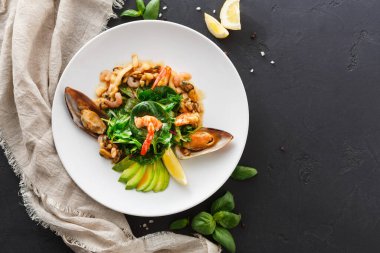 Bir deniz ürünleri tabağı, karides, midye ve yeşilliklerle birlikte beyaz bir tabağa yerleştirilir. Limon dilimleri yan yana dizilmiş. Ayar koyu bir yüzey ve yumuşak keten kumaş içeriyor..