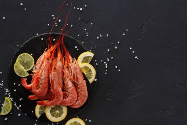 Siyah bir tabak birkaç büyük karidesi limon dilimlerinin yanında tutar. Tuz tabağın etrafına saçılmış. Sahne basit ve deniz ürünleri tabağına odaklı..