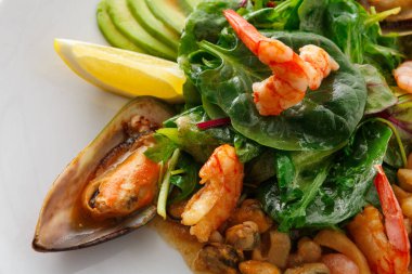 Bir tabak salatada taze sebzeler, karides, avokado dilimleri ve bir dilim limon var. Karides canlı karışıma karşı ışıldıyor. Sahne aydınlık ve yemek masasında davetkar..