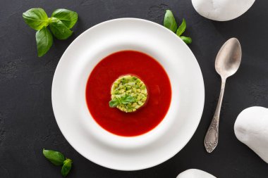 Yeşil süslemeli yemeğin yuvarlak bir kısmı beyaz bir tabakta kırmızı çorbanın ortasına konur. Tabağın etrafına taze fesleğen yaprakları yerleştirildi. Tabağın yanında bir kaşık var..