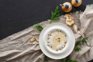 Bir tabak yemek desenli bir masa örtüsünün üzerinde duruyor. Konteynırlardaki baharatlarla birlikte küçük ekmek parçaları yakınlardadır. Yeşil otlar tabağın etrafına saçıldı. Ortam davetkar ve sıcak görünüyor..